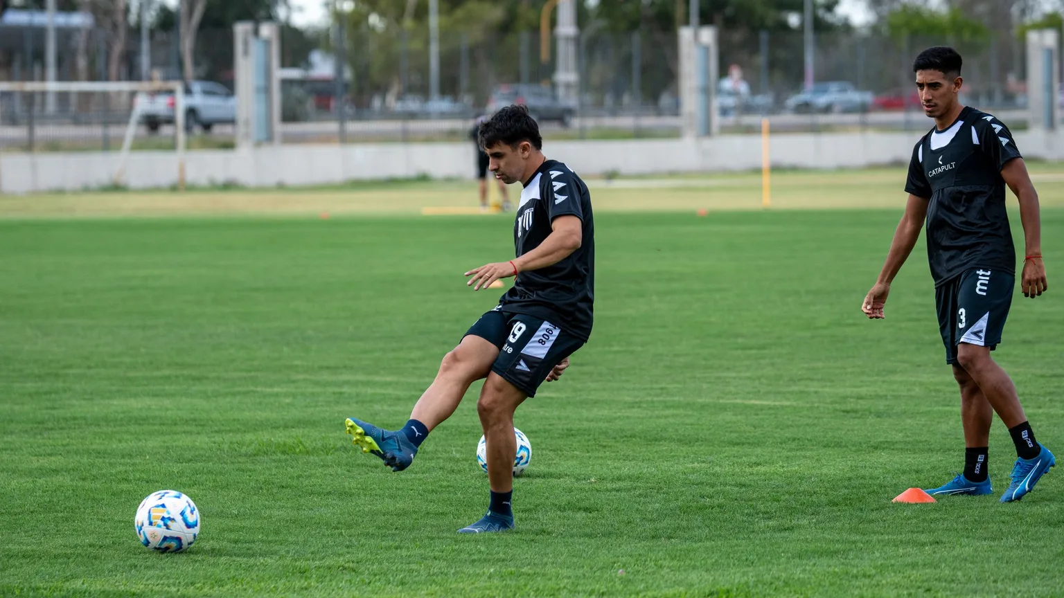 Young footballers working through a passing drill on a grass pitch.